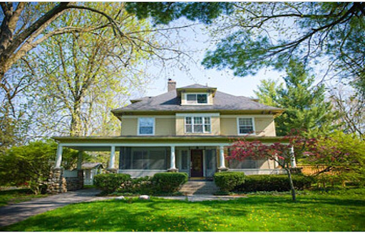 Mother Victor Flannery Hall, surrounded by greenery. It's a two story yellowish house with a wide porch