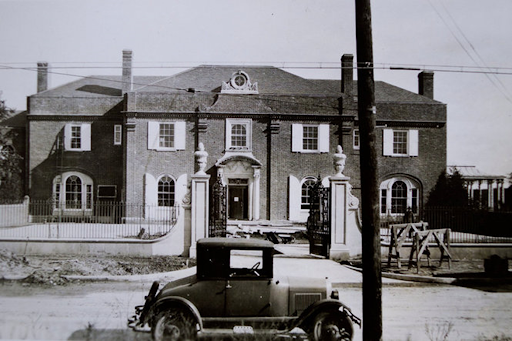 Black and white photo of the Brookby Estate with an early model of car parked out front. 
