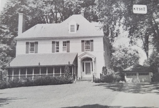 Black and white photo of Sister Mildred Hawkins Hall in Spring or Summer. The porch is closed in and features a long awning. A garage sits to the right.