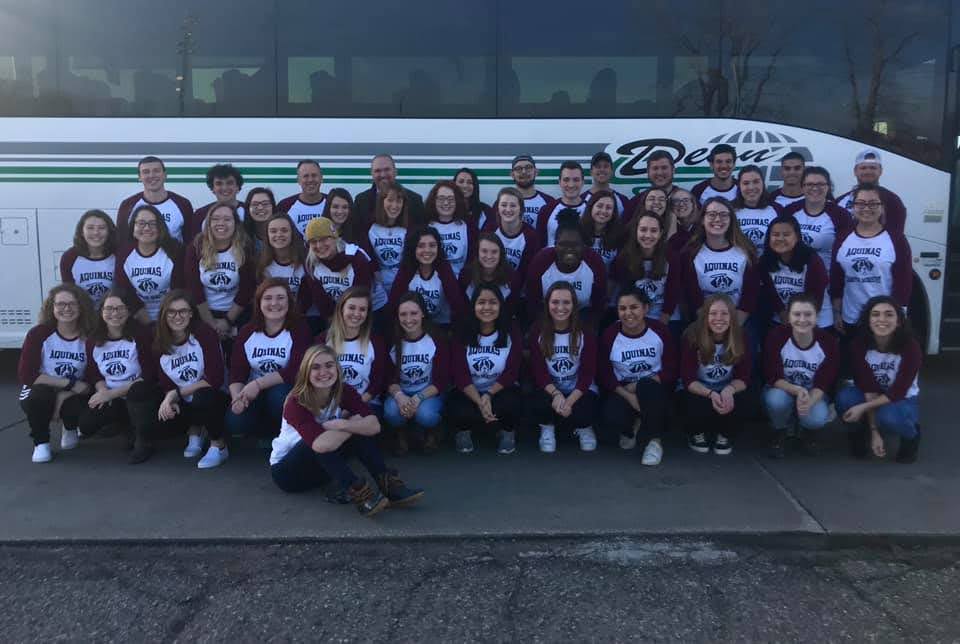 Large group of students wearing matching T-shirts in front of a large bus