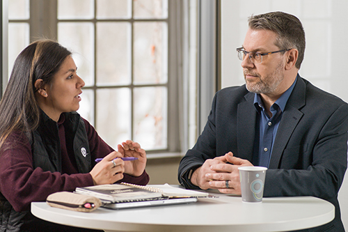 man and student talking at desk