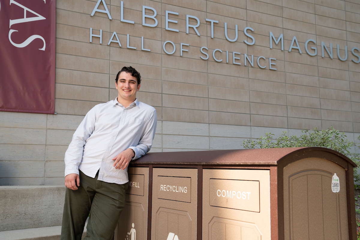 Aidan Donnelly beside waste collection bins outside of Albertus Magnus Hall of Science