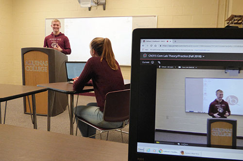 student speaking to another student at a podium while being recorded on a laptop