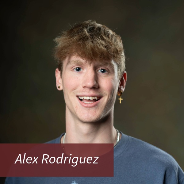 Headshot of a boy with blonde hair and a cross earring, in front of a brown background. Text reading: Alex Rodriguez, Writing Center Consultant.