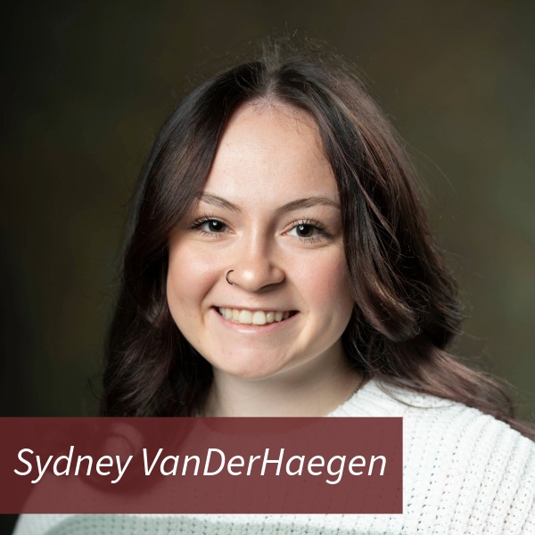Headshot of a girl with long, dark hair and a nose ring in front of a brown backdrop. Text reading: Sydney VanDerHaegen, Writing Center Consultant.