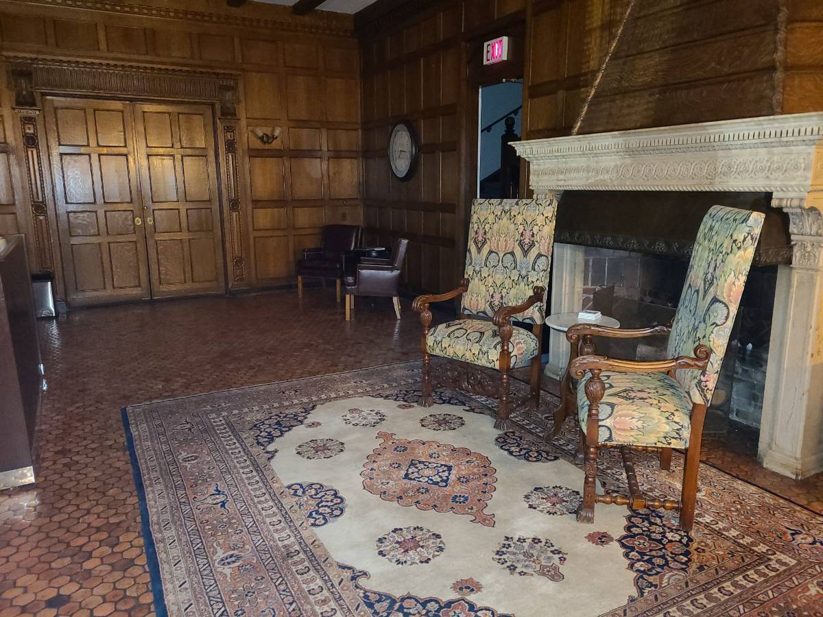 Holmdene Lobby, dark brown wood walls and tiled floors with two tall back soft chairs sitting in front of a grand fireplace