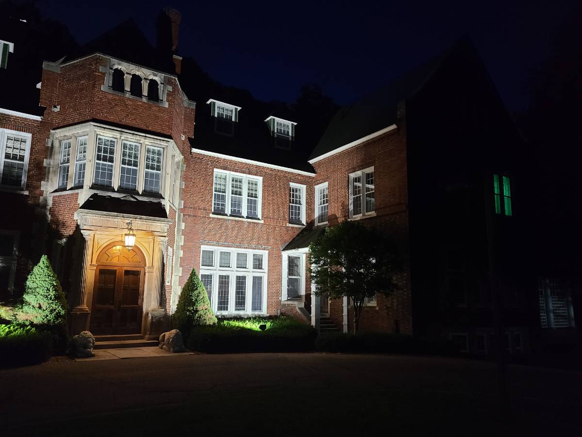 The front of Holmdene Manor at night, with up-lighting and a glowing green light in the window